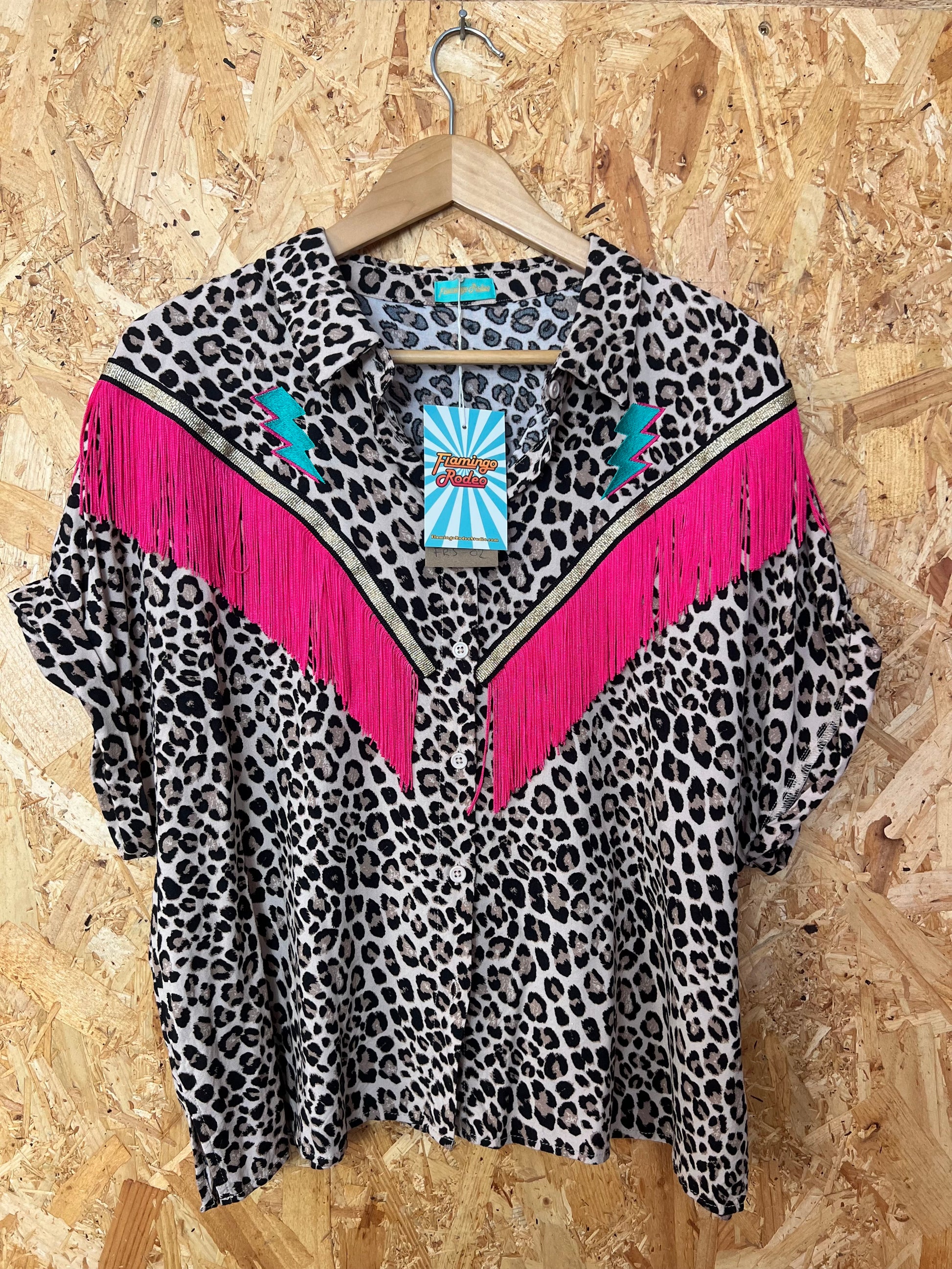 Leopard print top with pink fringe on a hanger against a wooden background by Flamingo rodeo