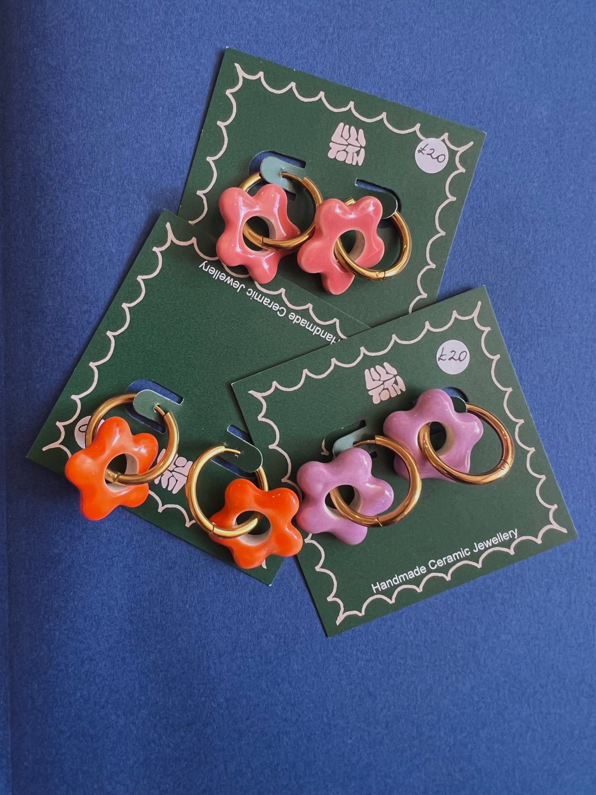 Pair of floral ceramic earrings on green cards against a blue background By Lili Toth