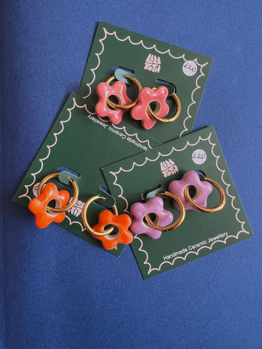 Pair of floral ceramic earrings on green cards against a blue background By Lili Toth